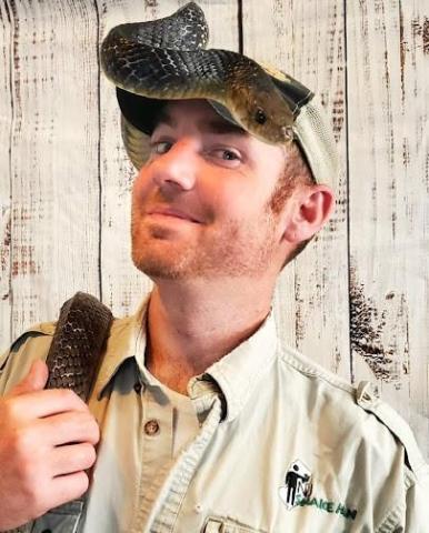 a photo of NJ Snake Man, a white man with a reddish beard, wearing a snake on his head and shoulder