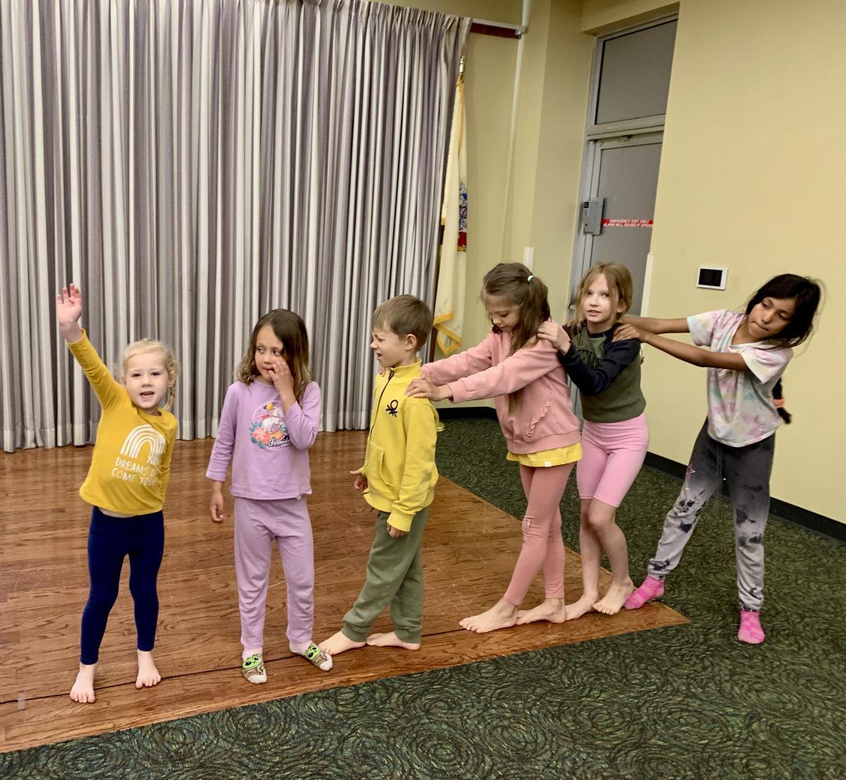 six young children doing a group yoga activity in a large room