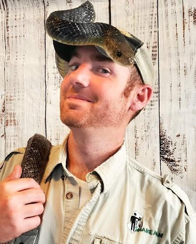 a photo of NJ Snake Man, a white man with a reddish beard, wearing a snake on his head and shoulder